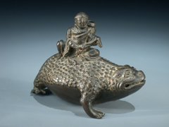  Bronze-Darstellung einer Kröte mit darauf sitzendem Einsiedler.